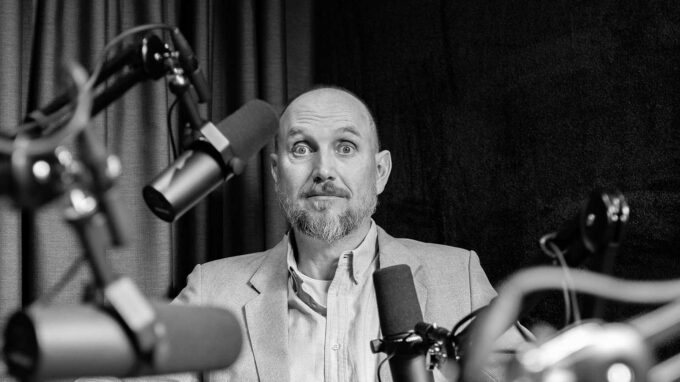 Man med massa mikrofoner framför sig och ser bekymrad ut.