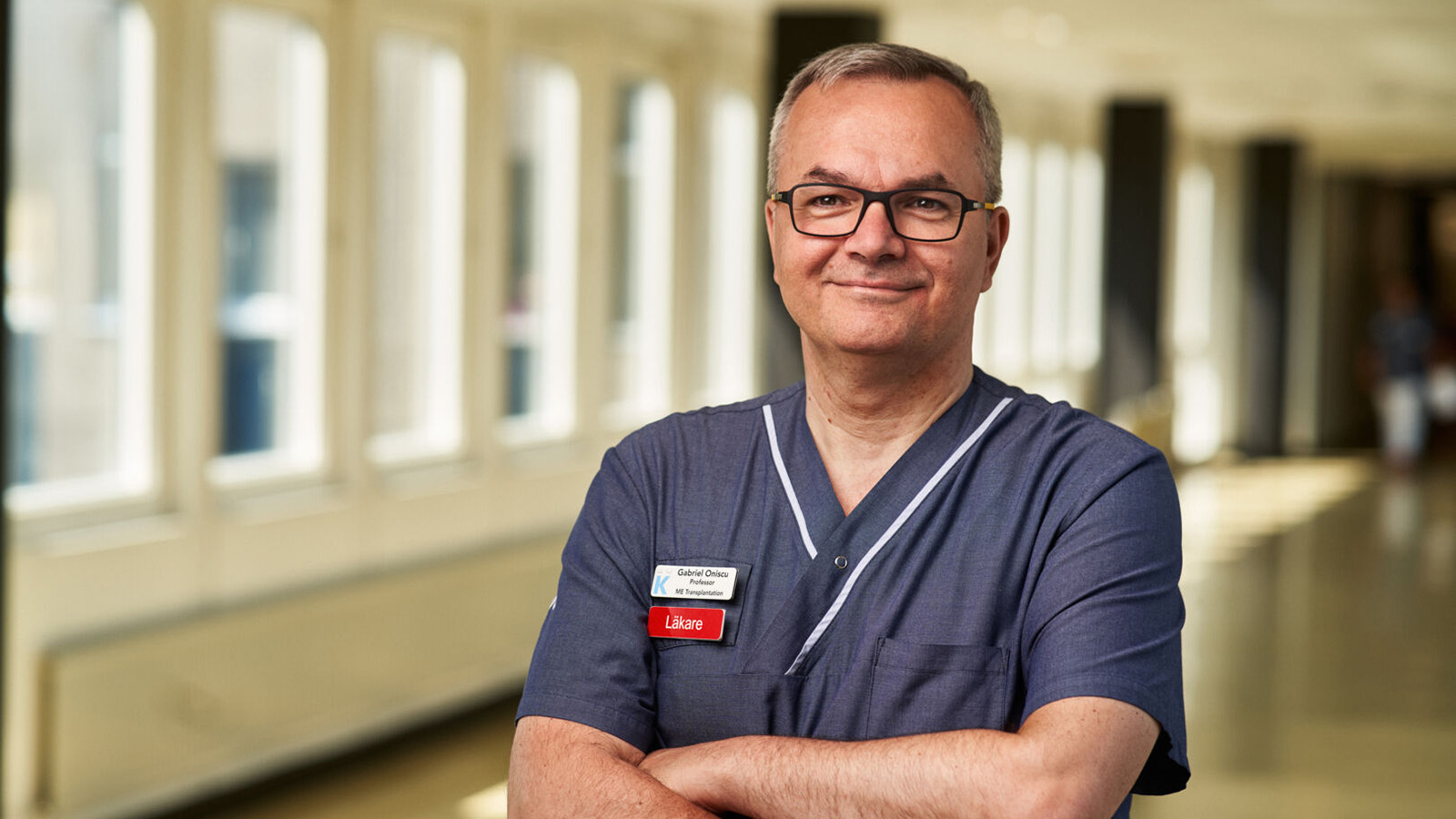 Läkare och man leer och tittar rakt in i kameran med armarna i kors.